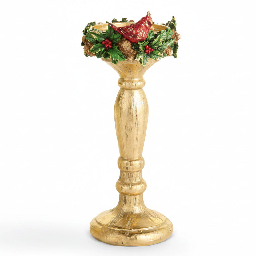 larger gold-colored holiday candle holder with a distressed finish, decorated with green holly leaves, red berries, pinecones, and a red cardinal at the rim, set against a plain white background.