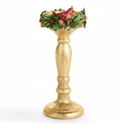larger gold-colored holiday candle holder with a distressed finish, decorated with green holly leaves, red berries, pinecones, and a red cardinal at the rim, set against a plain white background.