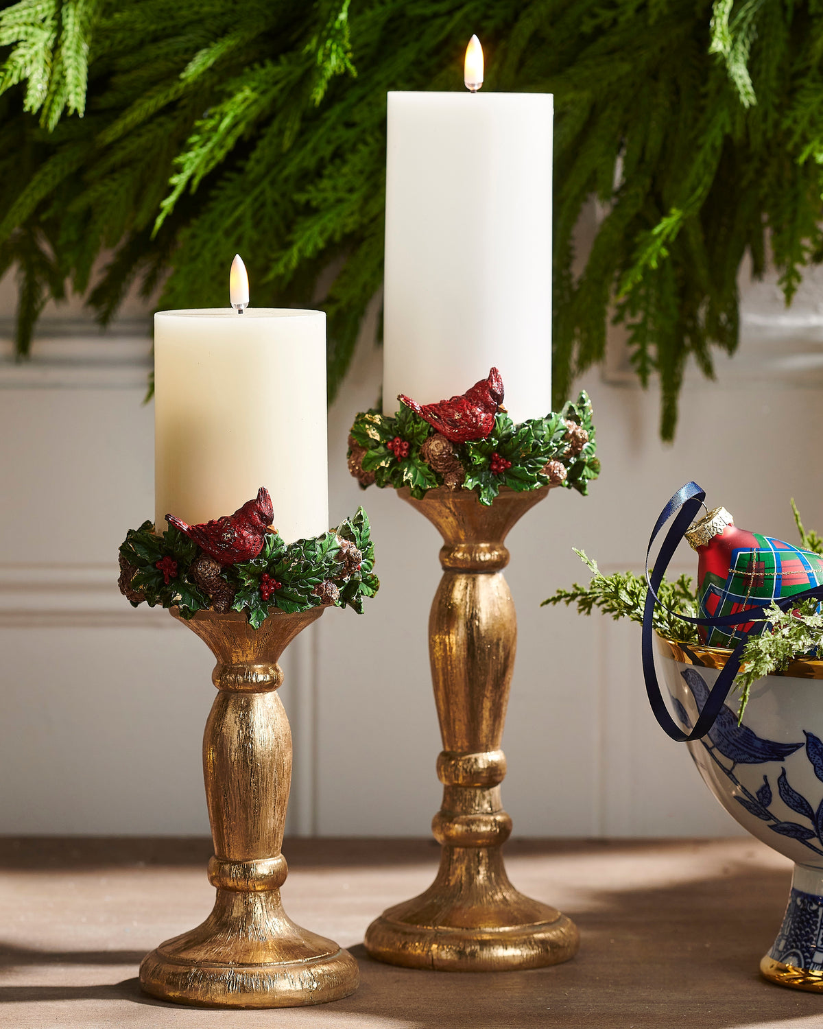 2 Cardinal Candlesticks with lit pillar candles on them in a decorated setting