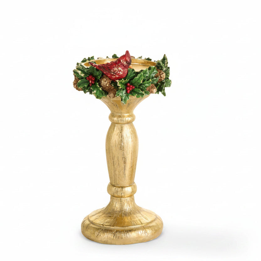 smaller gold-colored holiday candle holder with a distressed finish, decorated with green holly leaves, red berries, pinecones, and a red cardinal at the rim, set against a plain white background.
