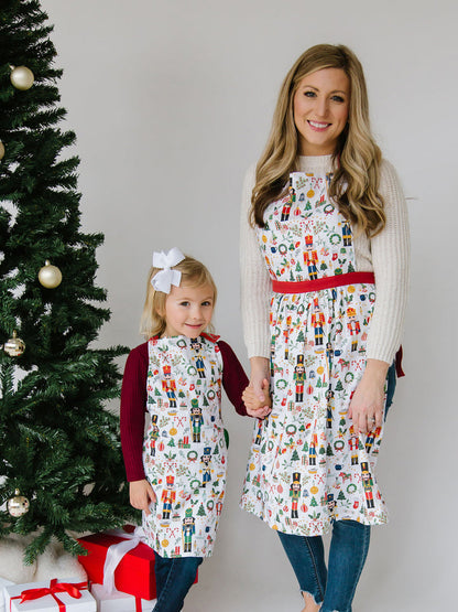 person and child each wearing nutcracker aprons and standing next to a christmas tree.