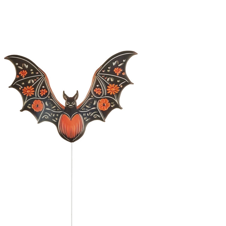A decorative bat-shaped garden stake with spread wings, a black body and wings decorated with orange floral motifs and a bright orange body
