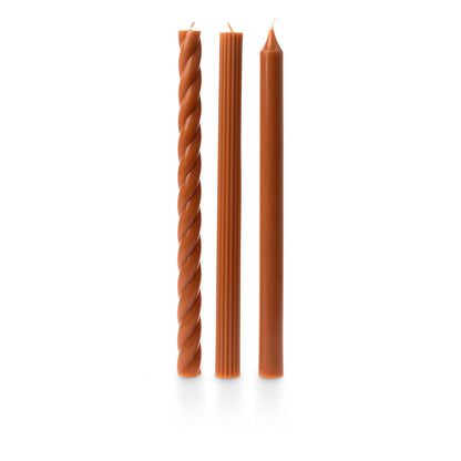 three assorted orange taper candles on a white background