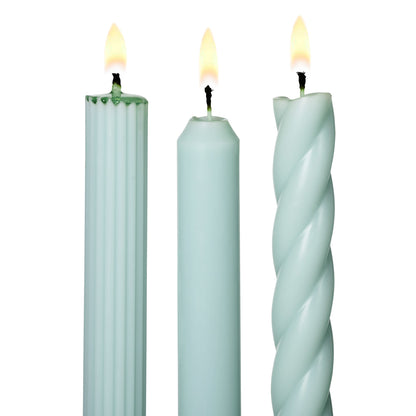 three lit assorted light blue taper candles on a white background