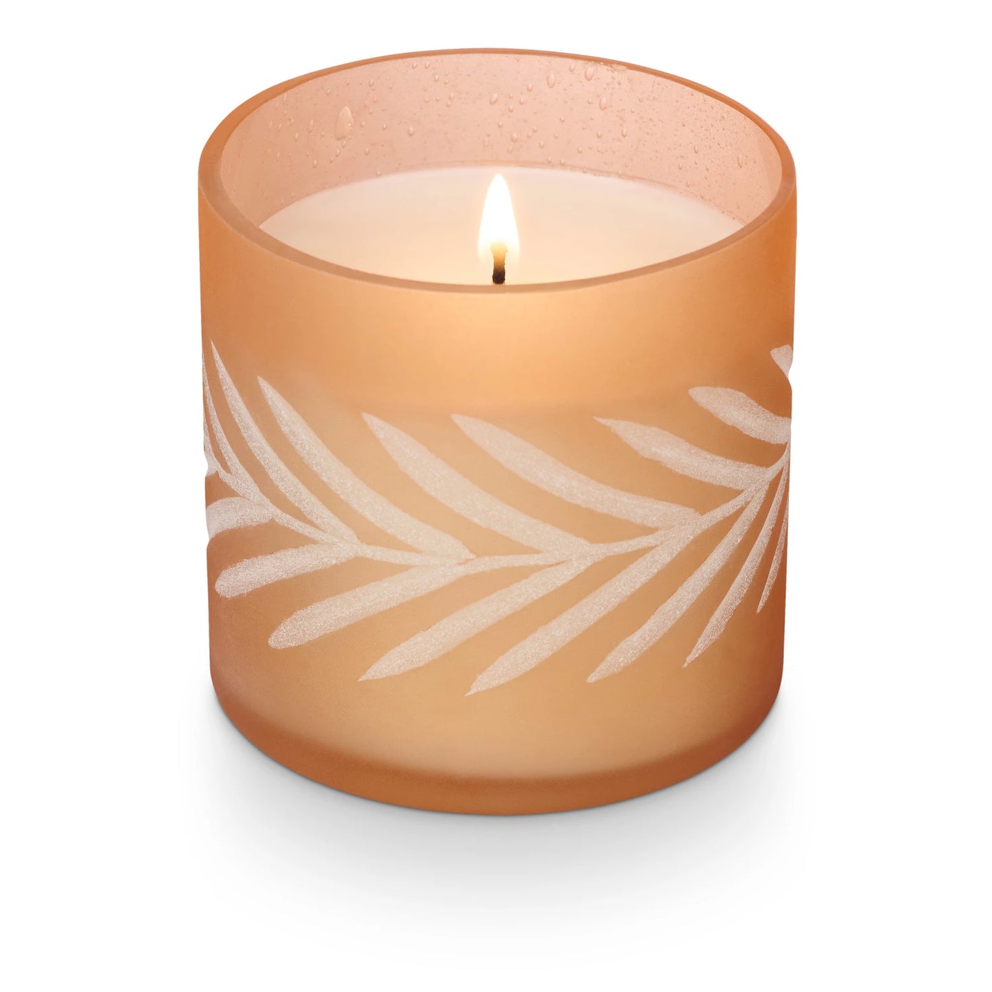 A soy wax candle in a frosted glass jar with a leaf pattern, with a lit flame.