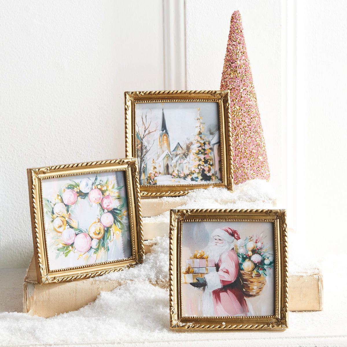 3 small gold framed art pieces arranged with artificial snow and a a holiday tree on a decorated table