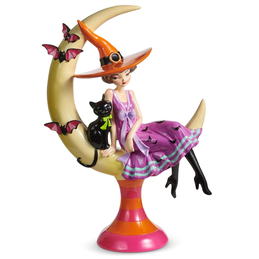 Figurine of a witch wearing a lavender dress and orange hat sitting on a Crescent moon with a black cat and bats fluttering around the moon.