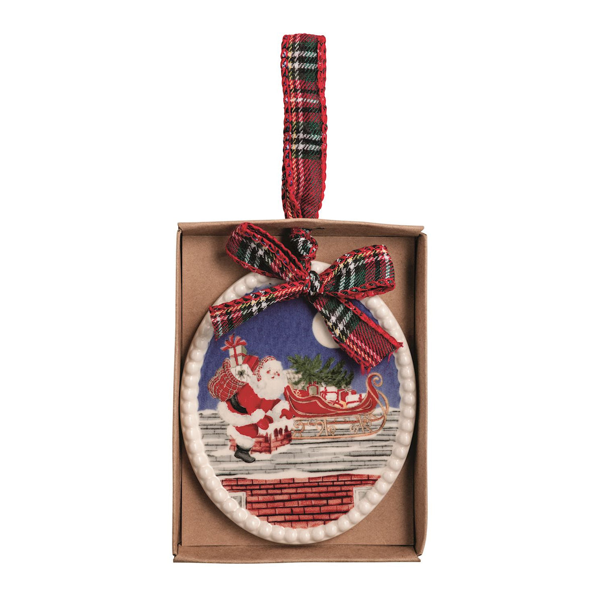 A Christmas ornament in its brown cardboard box, featuring an oval design with Santa Claus next to his sleigh on a rooftop against a blue night sky, accented with a red and green plaid ribbon bow and hanging loop.