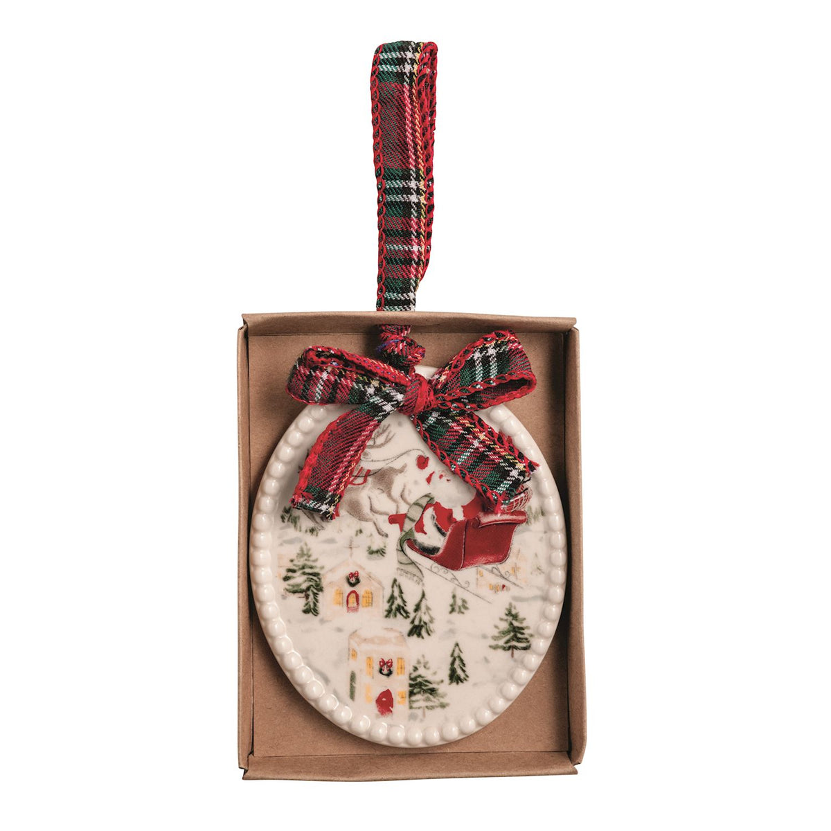 A ceramic Christmas ornament featuring a winter village scene with Santa in a sleigh flying above, displayed inside its brown gift box with a red plaid ribbon bow and hanging loop.