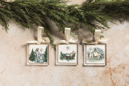 3 nativity inspired ornaments on a stone surface with evergreen branch