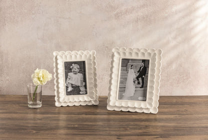 Two decorative white picture frames on a wooden surface with a neutral background