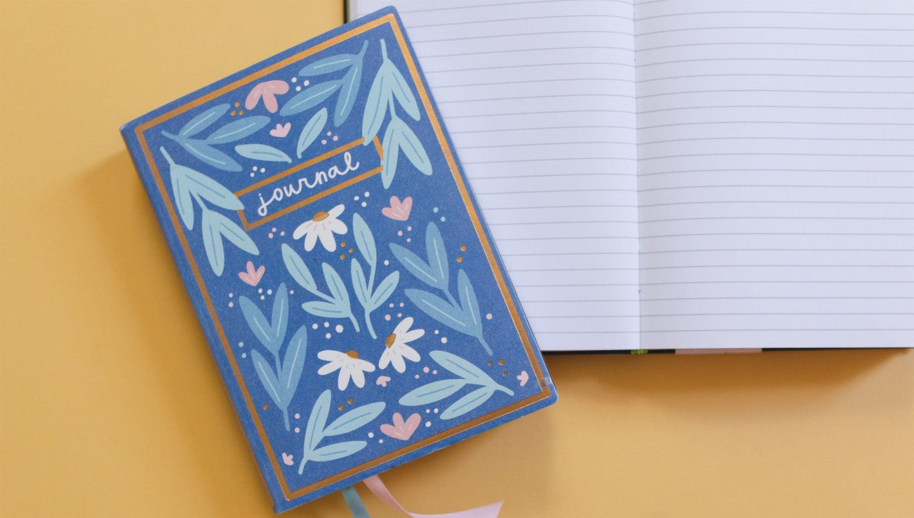 Blue Book Journal laying on an open Blue Book Journal on a light ornage background