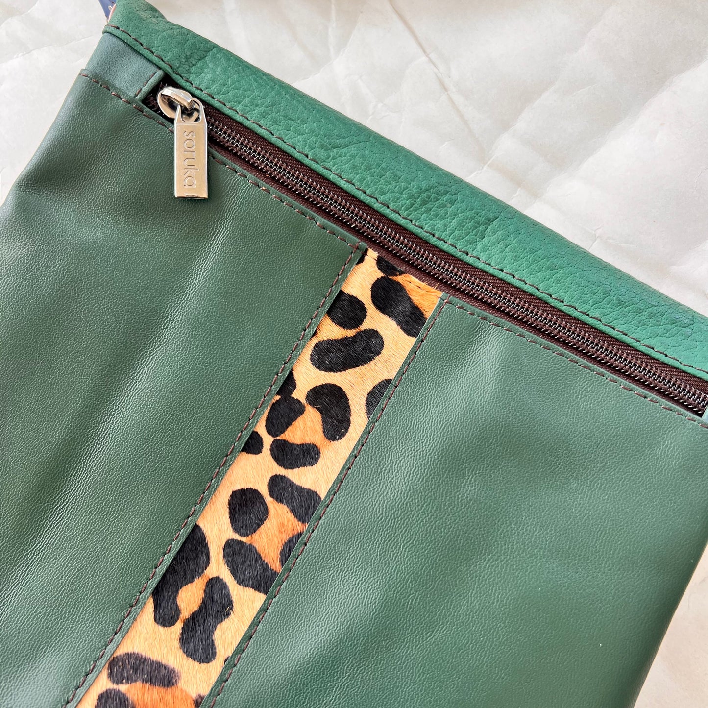 close-up of green greta bag with animal print stripe down the center and zipper at the top.