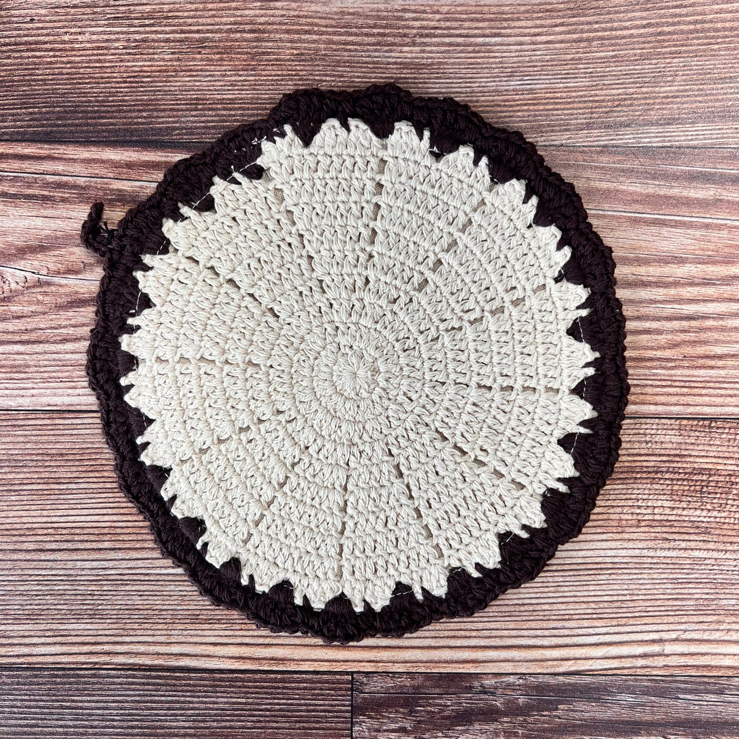off-white round crocheted pot holder with brown boarder. 