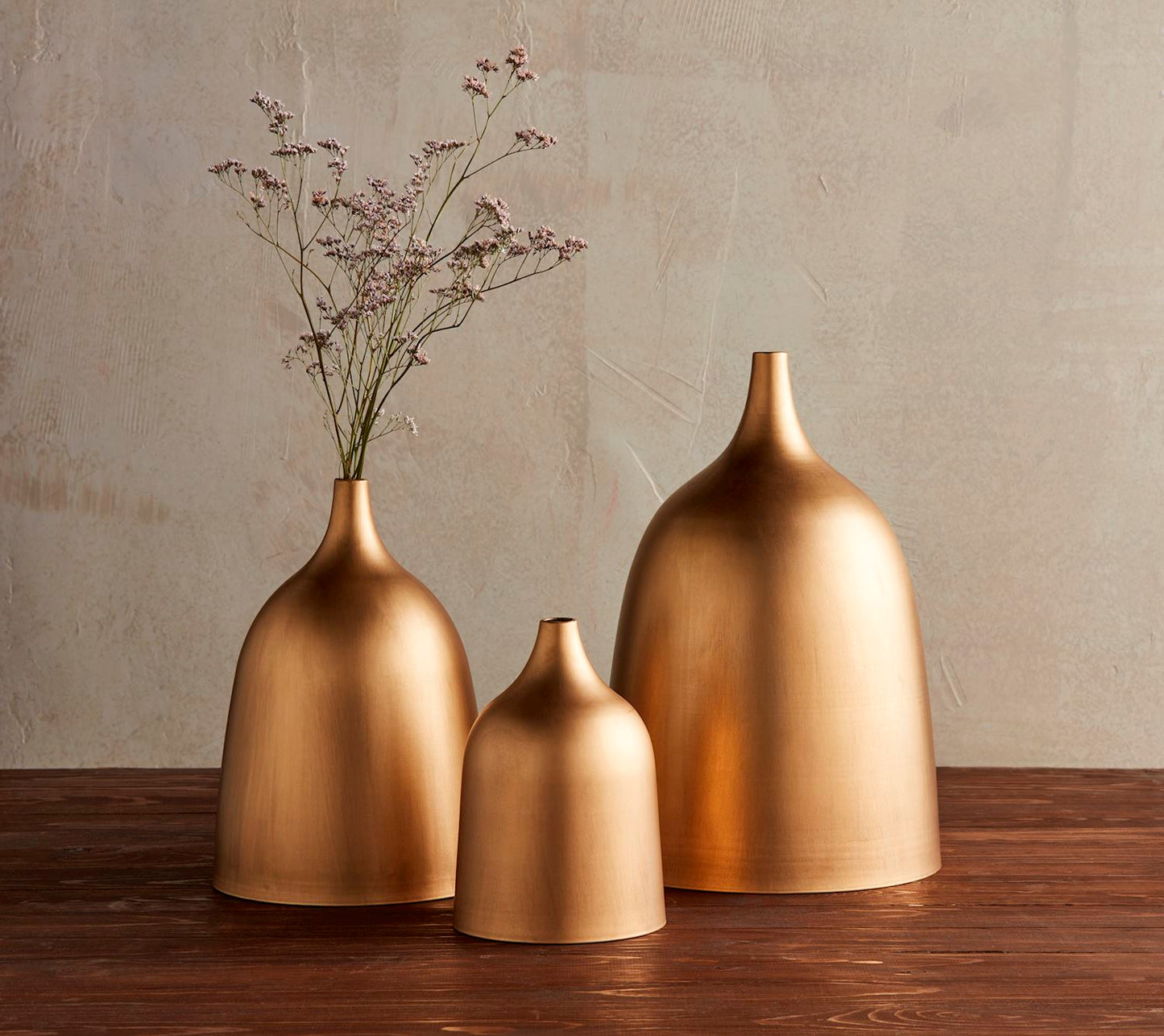 3 sizes of Brass Vases arranged on a table, medium vase has florals in it