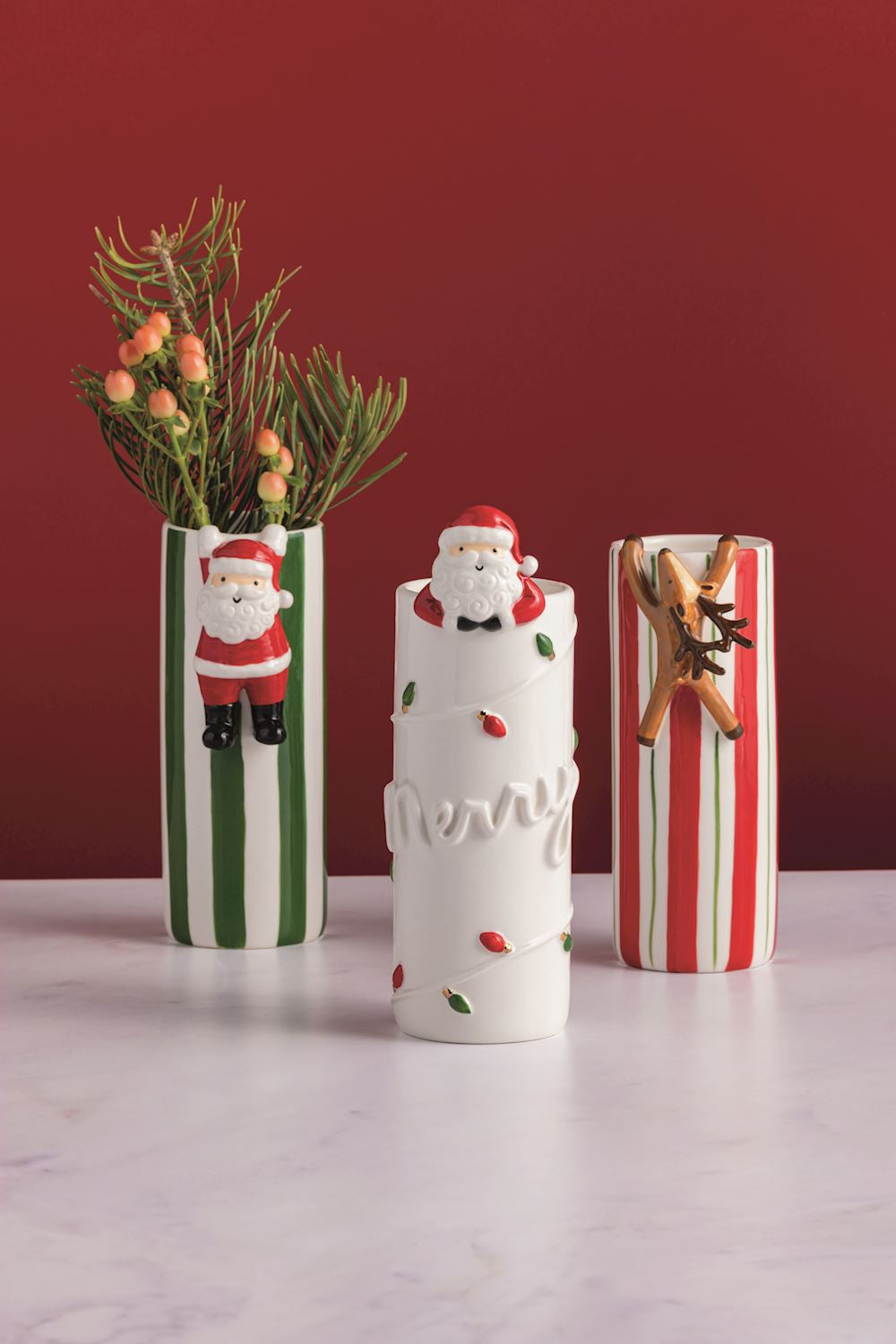 Three decorative vases with Christmas-themed designs on a white surface against a red background.