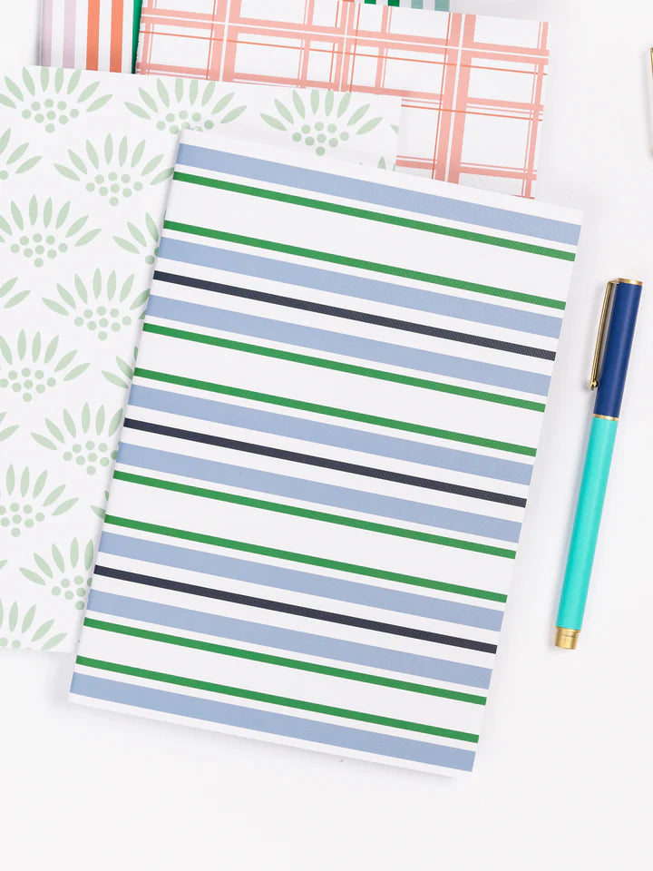 blue and green stripes notebook laying on a desk with a pen and other notebooks.