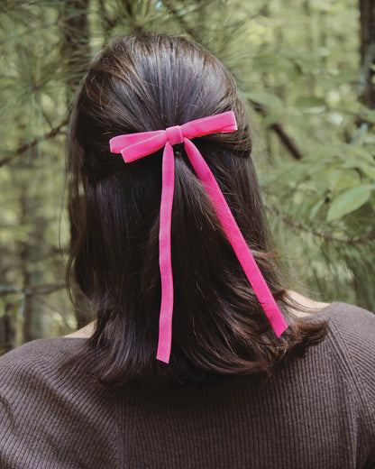 back of person with dark and a pink velvet bow clipped in a half up-half down hair style.