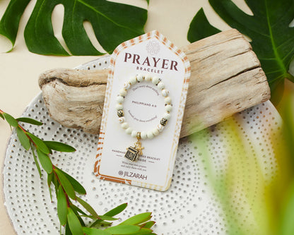 ivory beaded bracelet with gold cross and prayer box charms on card packaging.