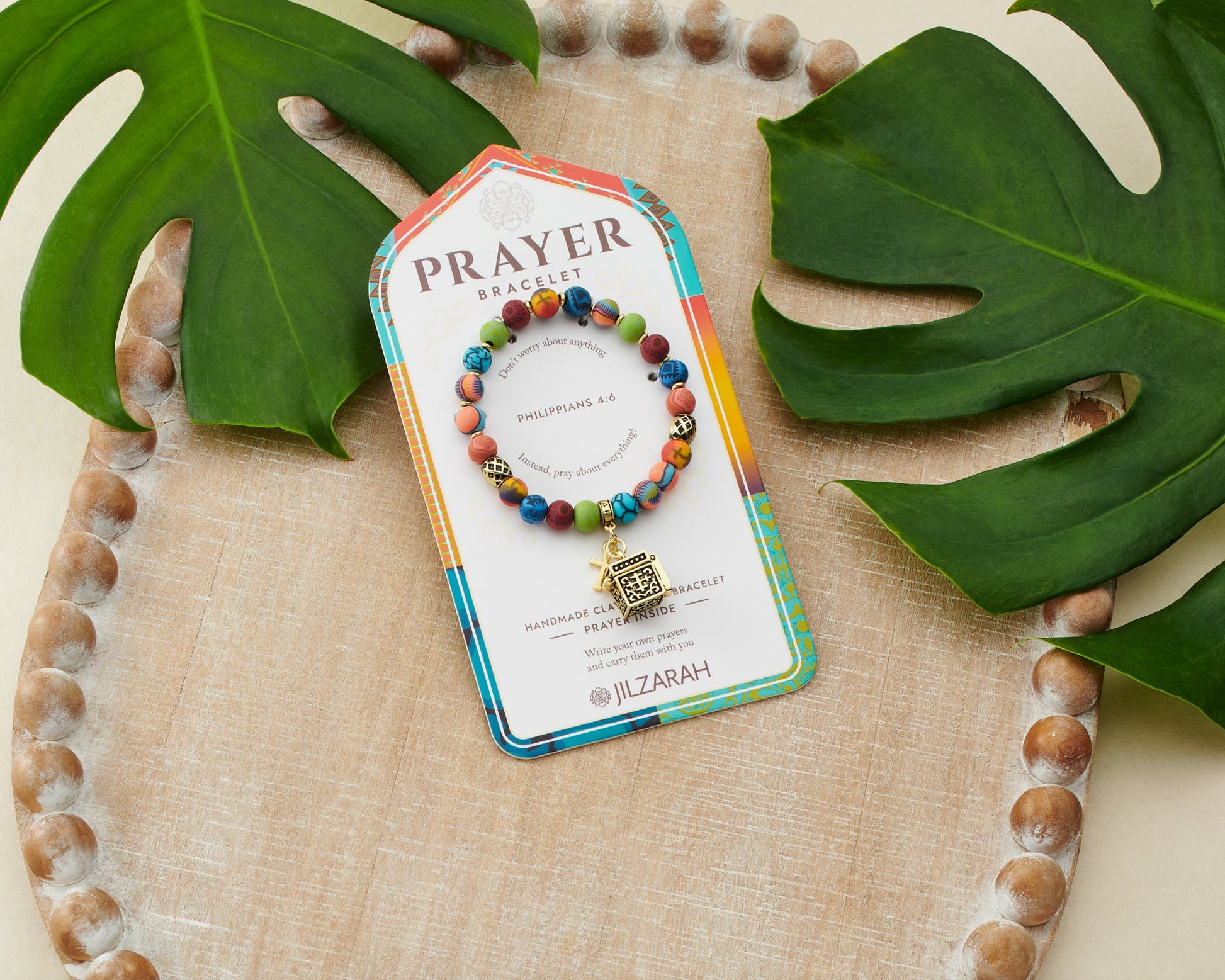 multi colored beaded bracelet with gold cross and prayer box charms on card packaging.