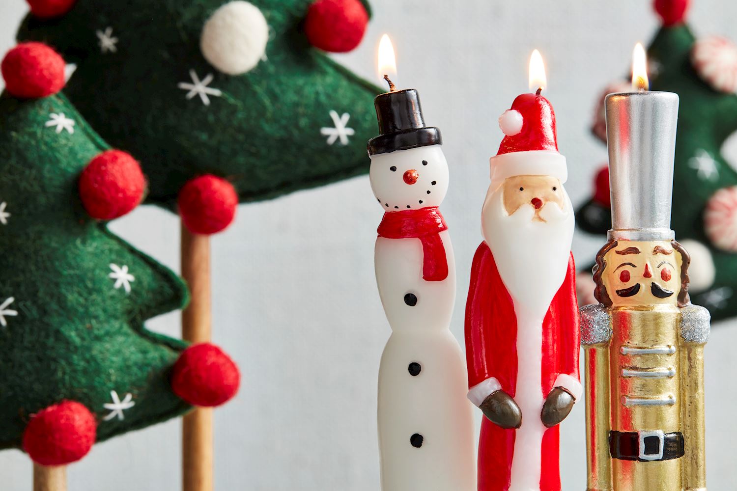 close-up of 3 lit taper candles with felt trees in the background.