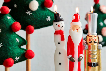 close-up of 3 lit taper candles with felt trees in the background.