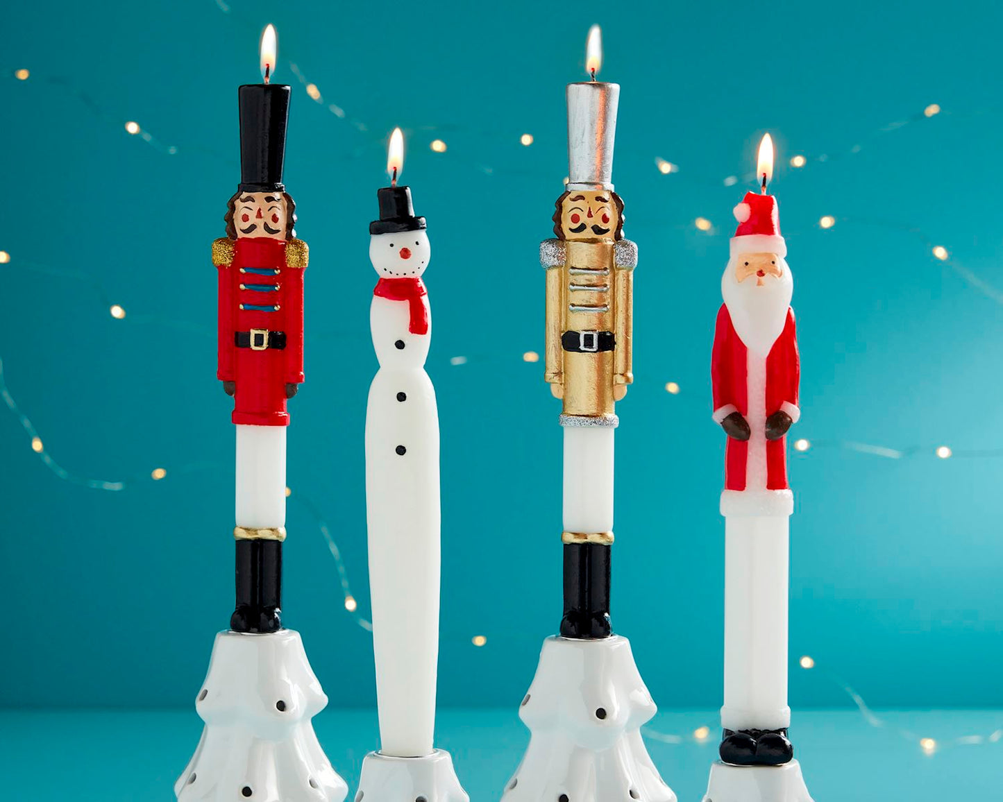 4 lit taper candles in a row, one each of a red nutcracker, snowman, gold nutcracker, and santa.