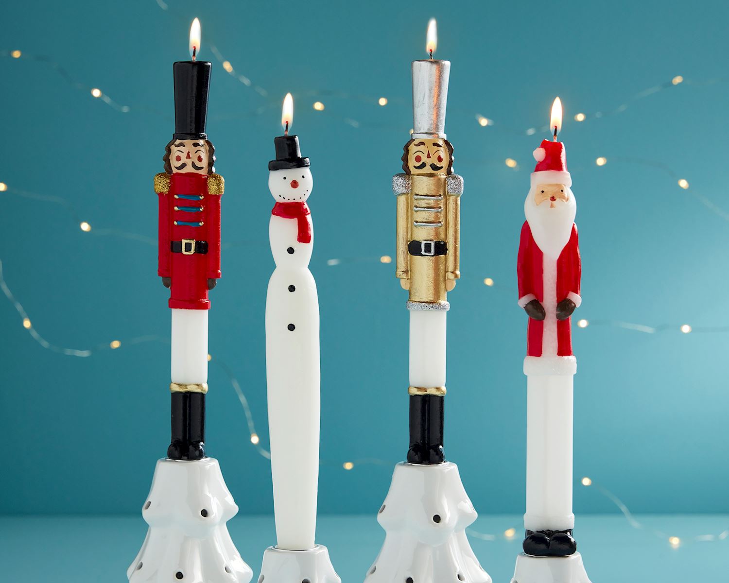 4 lit taper candles in a row, one each of a red nutcracker, snowman, gold nutcracker, and santa.