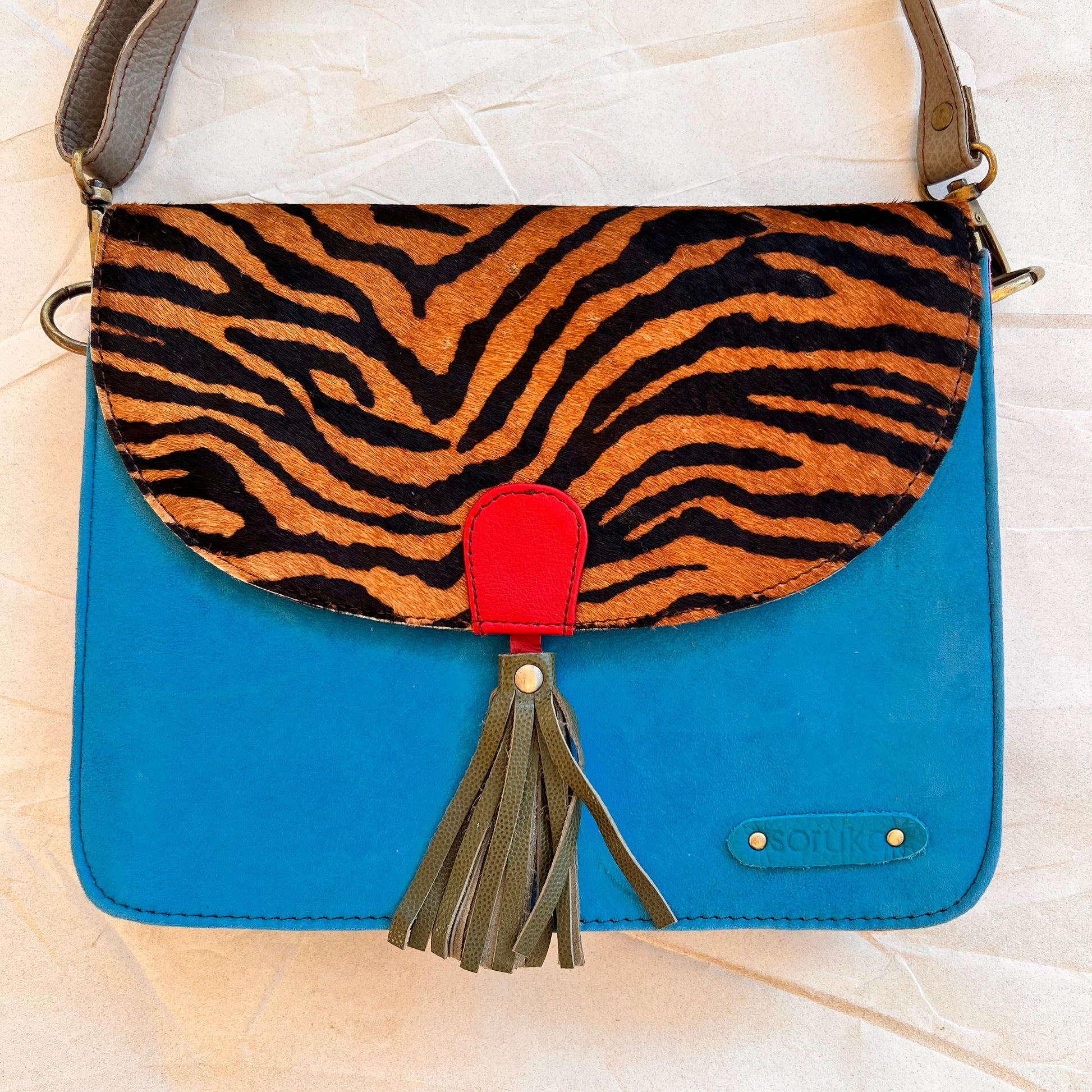 Front view of turquoise olivia handbag with striped print flap.