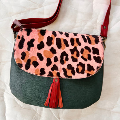lola bag with pink cheetah print hair-on-hide flap with rusty colored tassel over a deep green body.