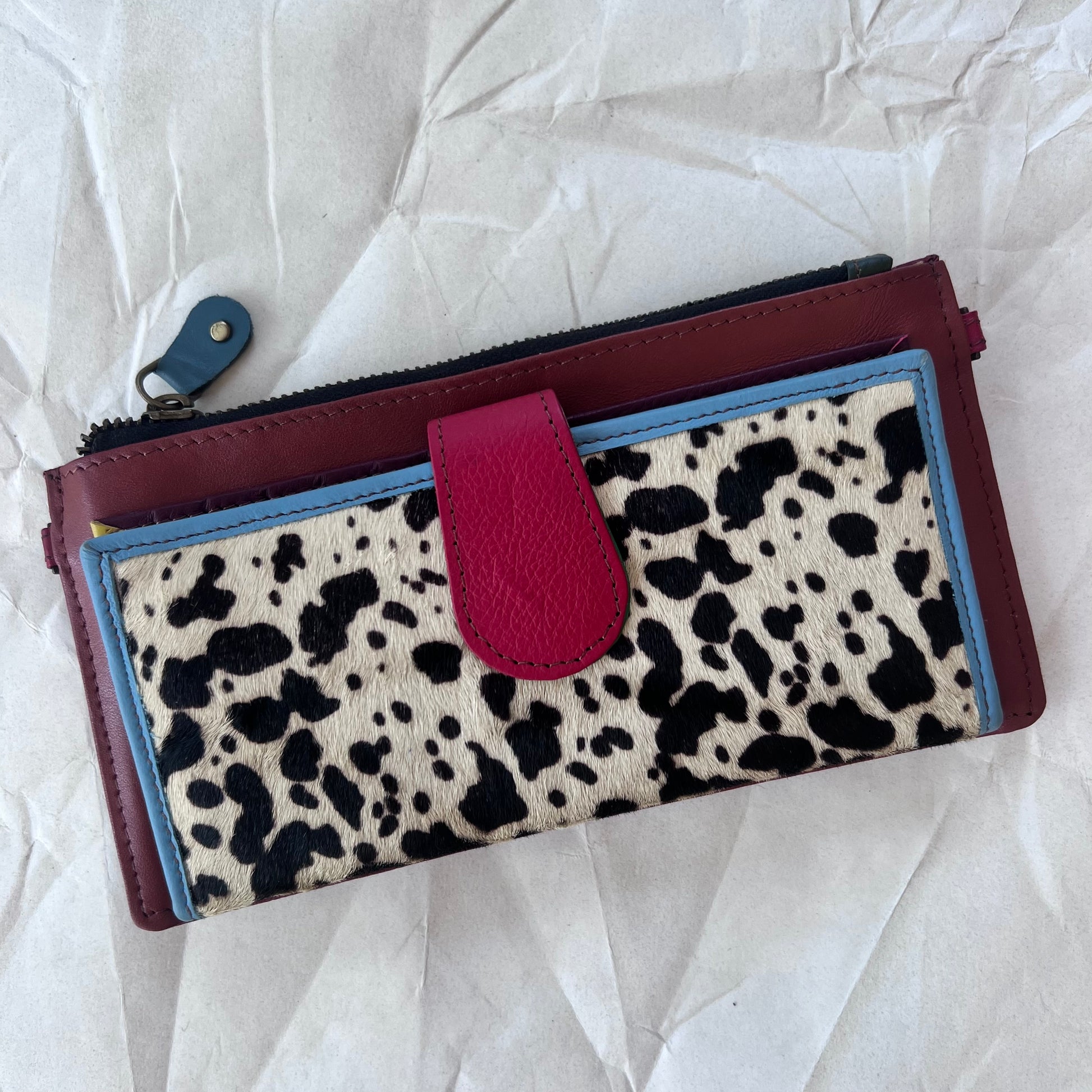 rectanglar dark red wallet with black and white spotted animal print pocket and red tab closure.