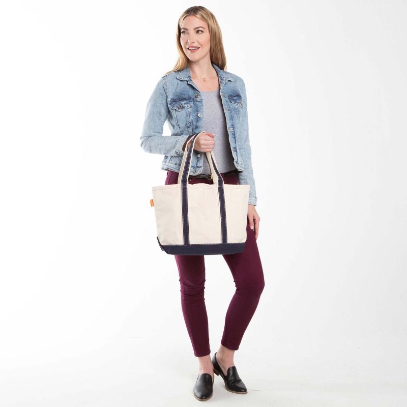 a person wearing maroon pants and denim jacket holding off white tote with navy blue trim and handles