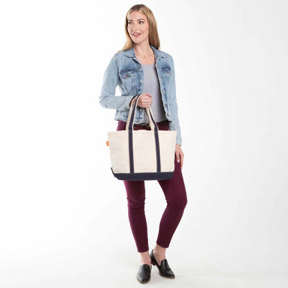 a person wearing maroon pants and denim jacket holding off white tote with navy blue trim and handles