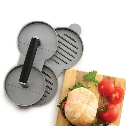 Top view of a white surface with the double burger press and a wooden board with a burger and sliced tomatoes on it