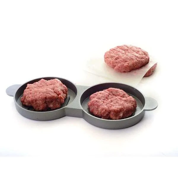 Double burger press with two uncooked burger patties in it and a stack of burger patties in the background