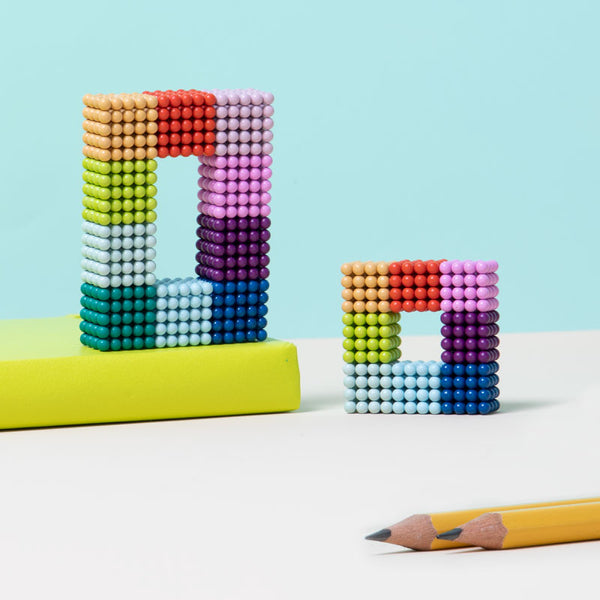 Matte Spectrum magnet balls in a rainbow of matte hues made into geometric shapes and set next to pencils and a book