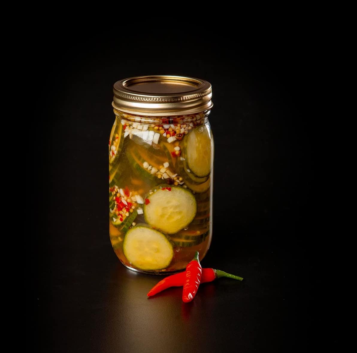 jar filled with pickled cucumbers with a pepper next to it.