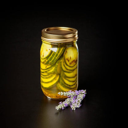 jar filled with pickled cucumbers with a sprig of lavender next to it.