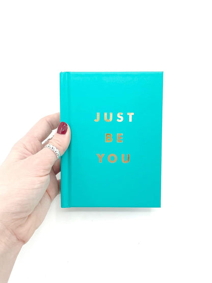 Turquoise book titled 'Just Be You' held by a hand on a white background