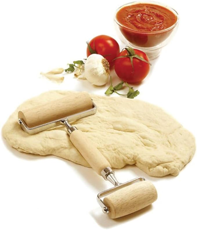 Wooden Pizza and Pastry Roller laying on a lump of dough with tomatoes, garlic, and a dish of sauce in the background