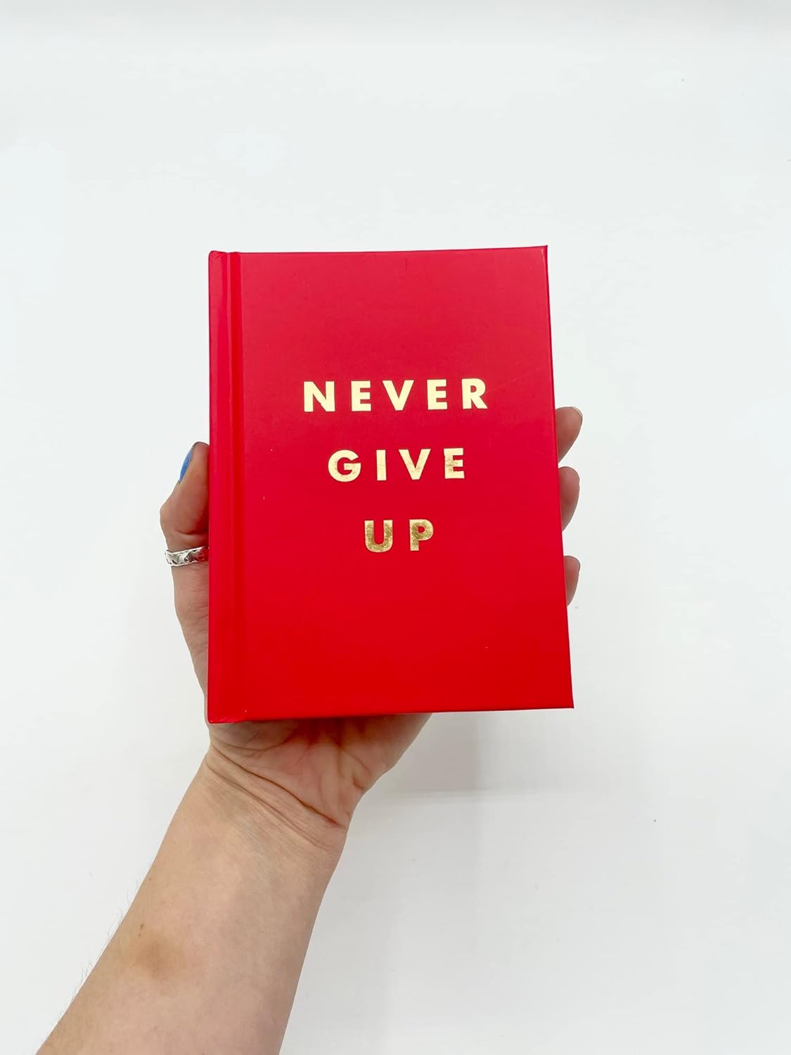 pink book with 'Never Give Up' text held by a hand on a white background