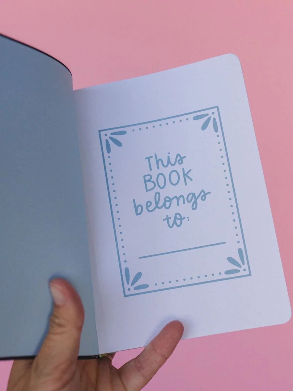a person holding a notebook open against a pink background