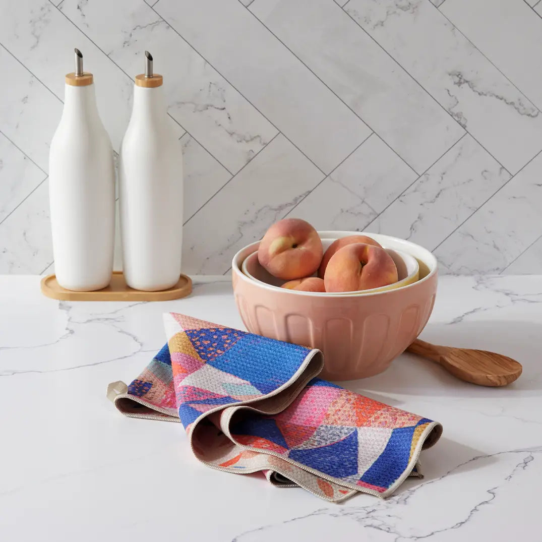 Birdsongs towel with patchwork side showing, draped on a counter next to a bowl of Peaches.