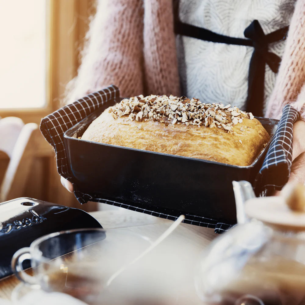 Person holding a loaf of bread in a pan with a cozy indoor setting