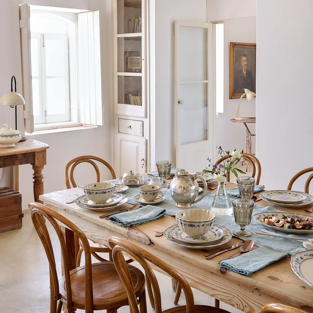 Dining room with a wooden table set for a meal, featuring silverware and vila beige and blue floral dishes.