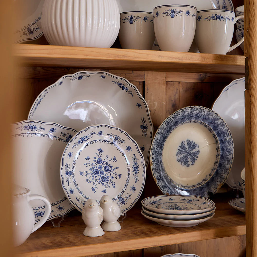 Collection of ceramic plates and cups with blue floral patterns on a wooden shelf.