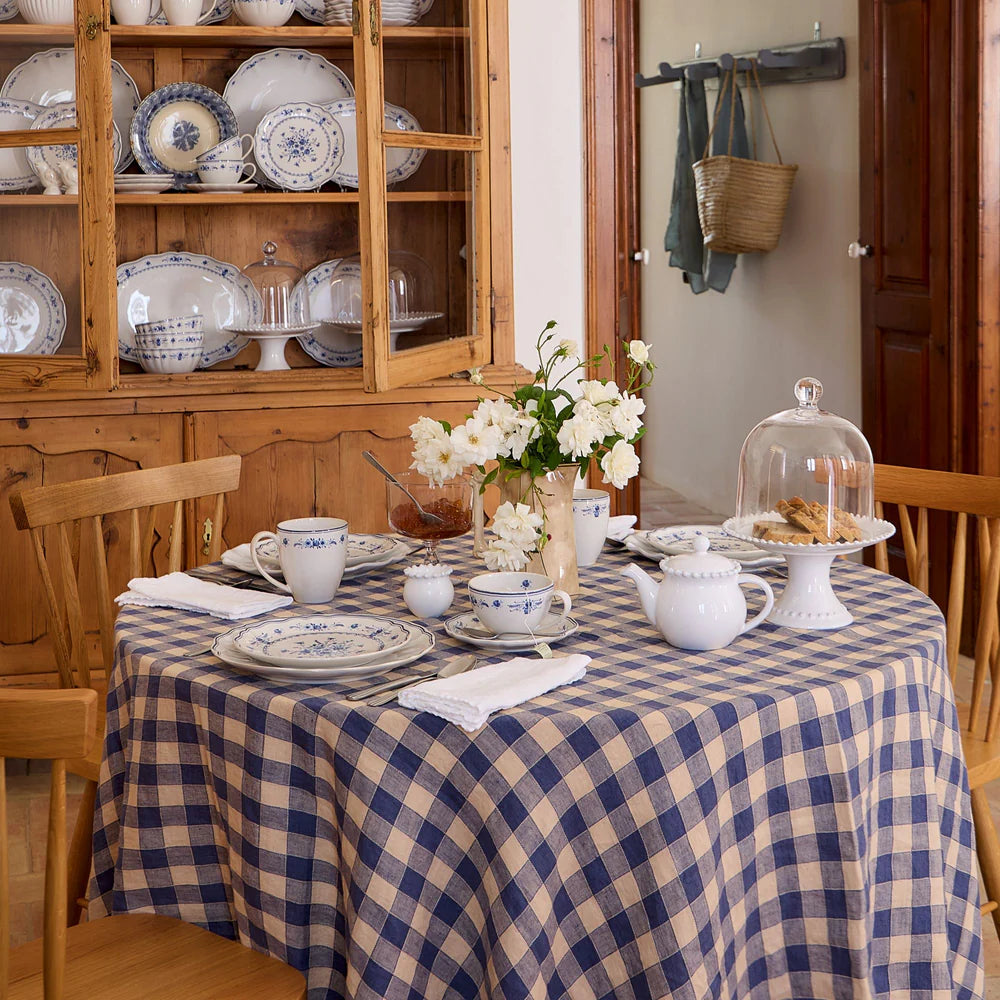 Dining room with a table set with white and blue floral dishes, a wooden cabinet with same dishes, and a vase of flowers.