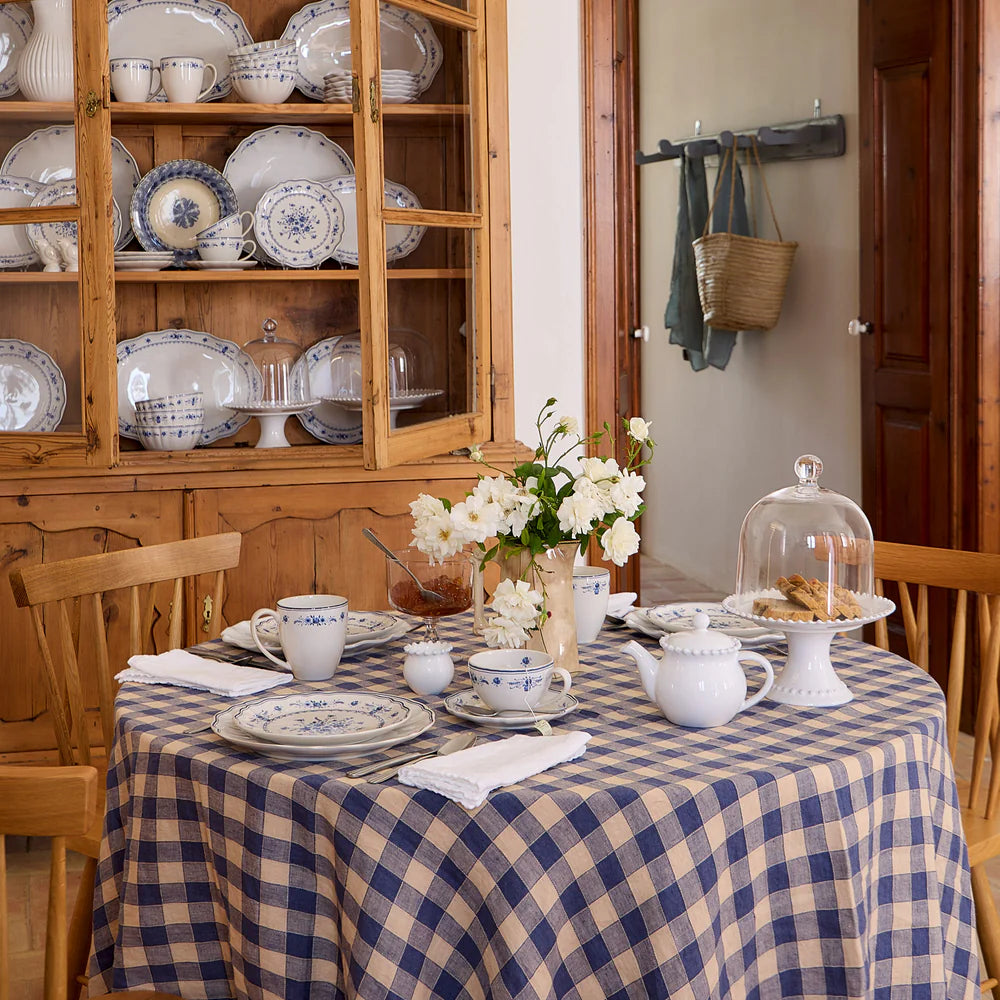 vila white and blue tea cup with saucer on a decorated table with a blue check cloth and a variety of plates and a tea pot