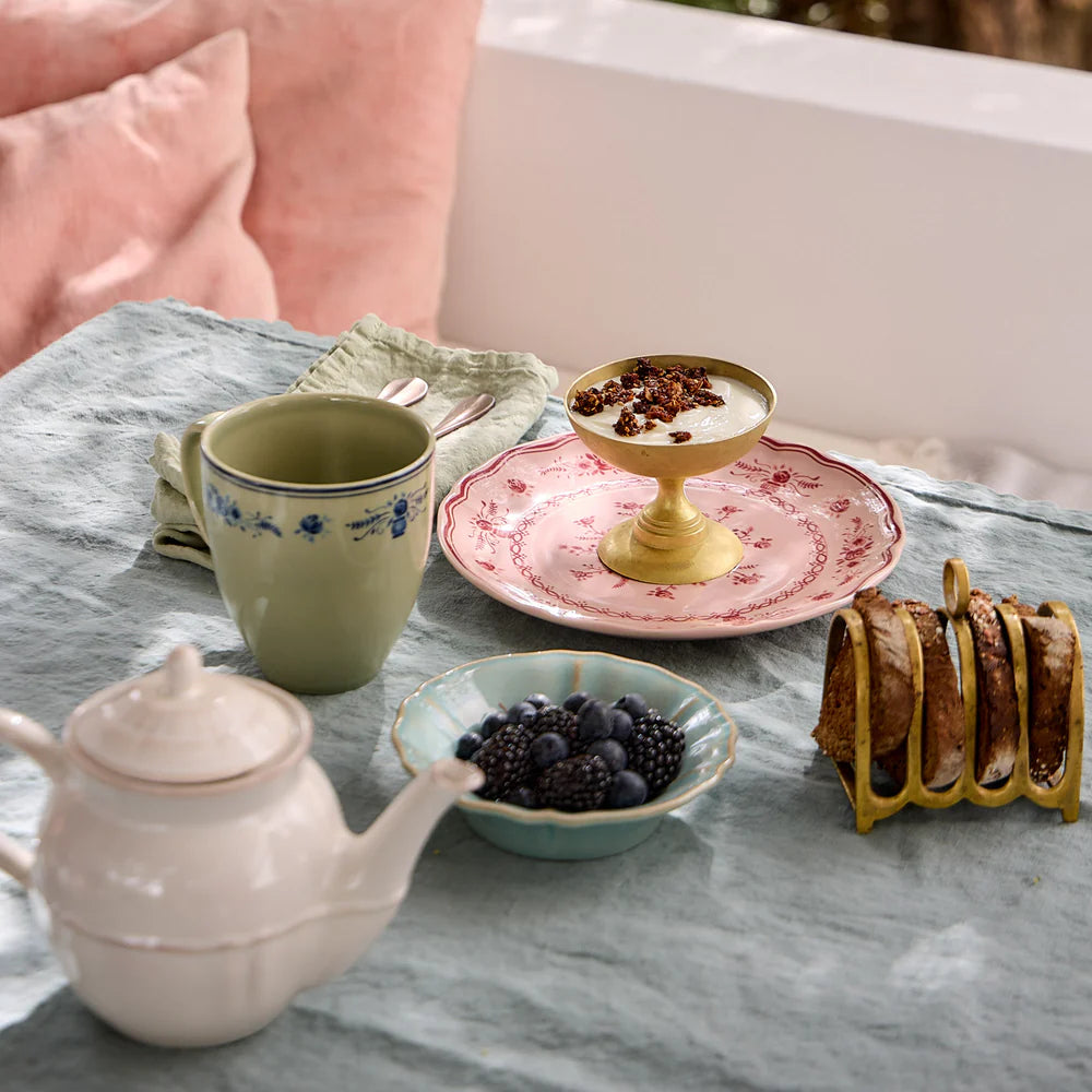Tea set with teapot, green and blue floral mug, and bowls on a marble surface