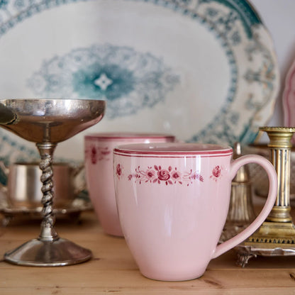 Pink mug with floral pattern on a wooden surface with decorative items.